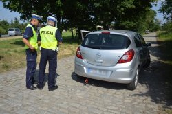 dwóch umundurowanych policjantów Wydziału Ruchu Drogowego kontroluje srebrny samochód osobowy.