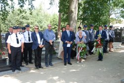 zdjęcie wykonane na cmentarzu, przedstawia umundurowanych policjantów i strażaków, oraz zaproszonych na uroczystość gości, kobieta i mężczyzna trzymają w ręce wiązanki kwiatów