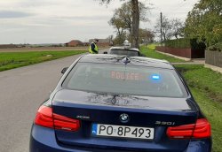 Policjanci Wydziału Ruchu Drogowego kontrolują pojazd na poboczu drogi. Na pierwszym planie nieoznakowany radiowóz BMW