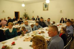 Na sali parafialnej przy stołach siedzą uczestnicy noworocznego spotkania z księdzem.